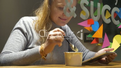 Woman in cafe eating ice-cream and using pad