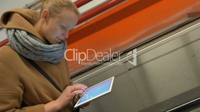 Woman on escalator using tablet computer