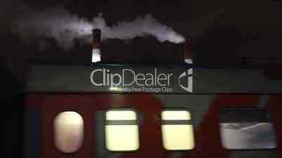 Passenger train passing by factory at night