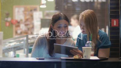Female friends talking and using touch pad in cafe
