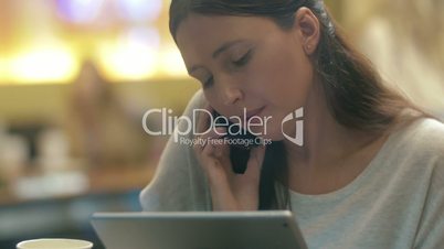 Woman busy with phone talk and using pad in cafe