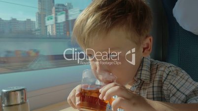 Child having tea and looking out window in moving train