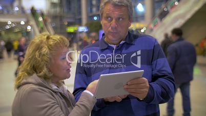 Senior couple having vivid talk using pad at the airport