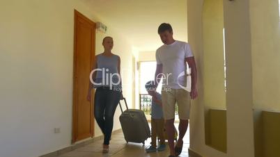 Family with rolling bags in hotel corridor