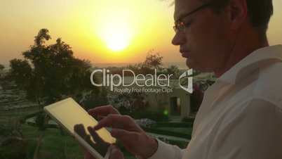 Businessman on vacation using touch pad at sunset