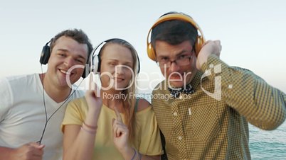 Excited trio enjoying music in headphones outdoor