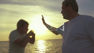 Two men having boxing workout on the beach at sunset