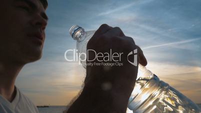 Man drinking fresh water from the bottle at sunset