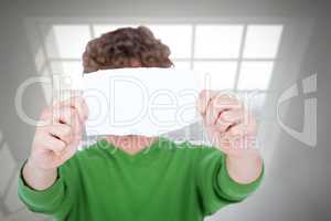 Composite image of man holding blank paper in front on face