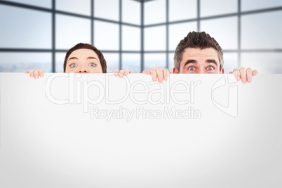 Composite image of man and woman hiding behind a white board wit