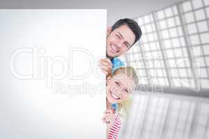 Composite image of smiling young couple hiding behind a blank si