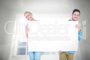 Composite image of smiling young couple holding a blank sign