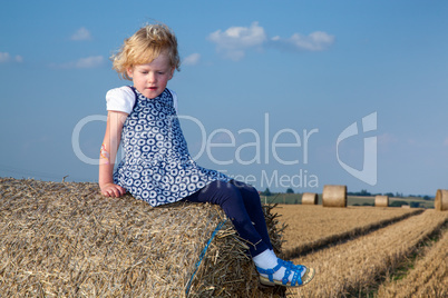 Girl sitting on straw roll on field