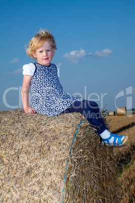 Girl sitting on straw roll on field