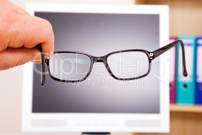 Hand holding glasses in front of computer screen