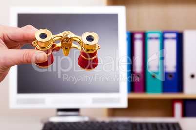 Hand holding binoculars in front of computer screen