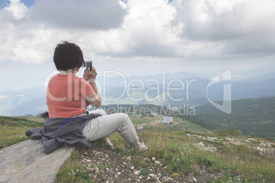Senior woman taking photos with smartphone on the mountain