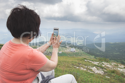 Senior woman taking photos with smartphone on the mountain