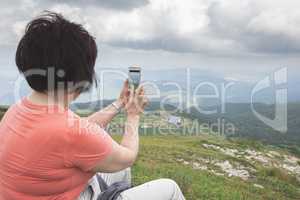 Senior woman taking photos with smartphone on the mountain