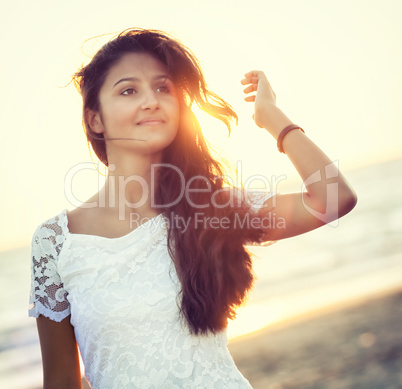 Beautiful young teenager with a white dress on the beach at suns