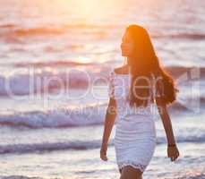 Beautiful young teenager with a white dress on the beach at suns