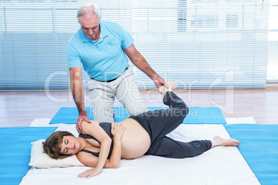 Therapist giving treatment to pregnant woman lying on mattress