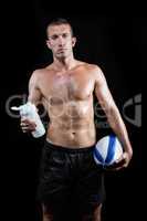 Shirtless man holding bottle and ball