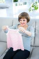 Smiling pregnant woman holding baby clothes