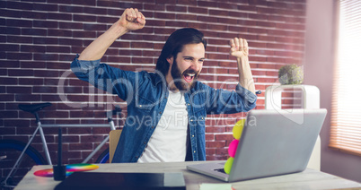 Cheerful creative businessman with arms raised looking at laptop
