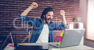Cheerful creative businessman with arms raised looking at laptop