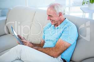 Senior man using digital tablet while sitting on sofa