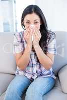 Pretty brunette looking at camera and sneezing on couch