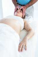 Calm pregnant woman receiving reiki treatment