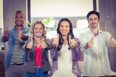 Portrait of business people giving thumbs up in office