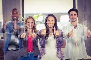 Portrait of business people giving thumbs up in office