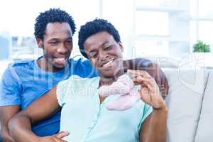 Happy couple looking at baby shoes while sitting on sofa