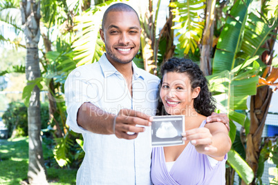 Portrait of happy man with pregnant wife holding sonogram