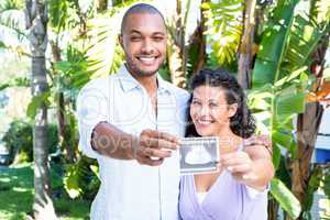 Portrait of happy man with pregnant wife holding sonogram