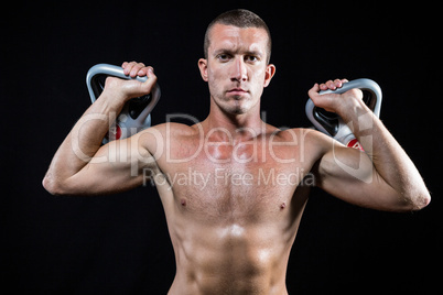 Confident shirtless athlete holding kettlebells