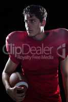 Serious American football player looking away holding ball