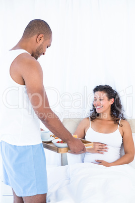 Husband with breakfast tray for happy pregnant wife