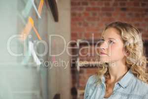 Businesswoman looking at glass board in creative office