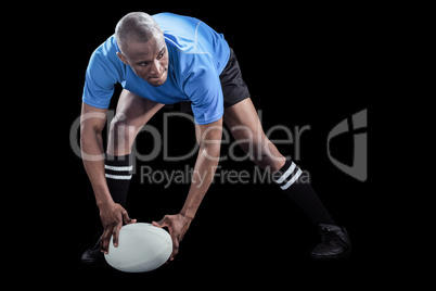 Sportsman bending and holding ball while playing rugby