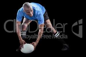 Sportsman bending and holding ball while playing rugby