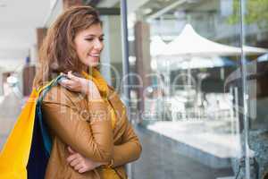 Smiling woman holding shopping bags and looking at window