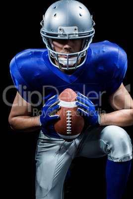 Determined American football player holding ball while kneeling