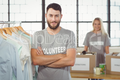 Portrait of happy man with arms crossed standing by clothes rack