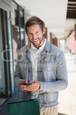 Young happy smiling man holding shopping bags and his mobile