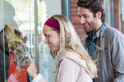 Smiling couple going window shopping and pointing at clothes