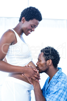 Affectionate husband kissing belly of his pregnant wife